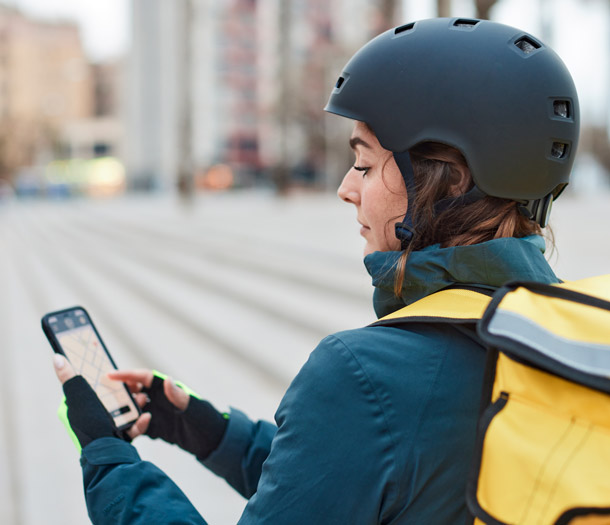 Junge Frau mit Fahrradhelm bedient das Display eines Mobiltelefons.