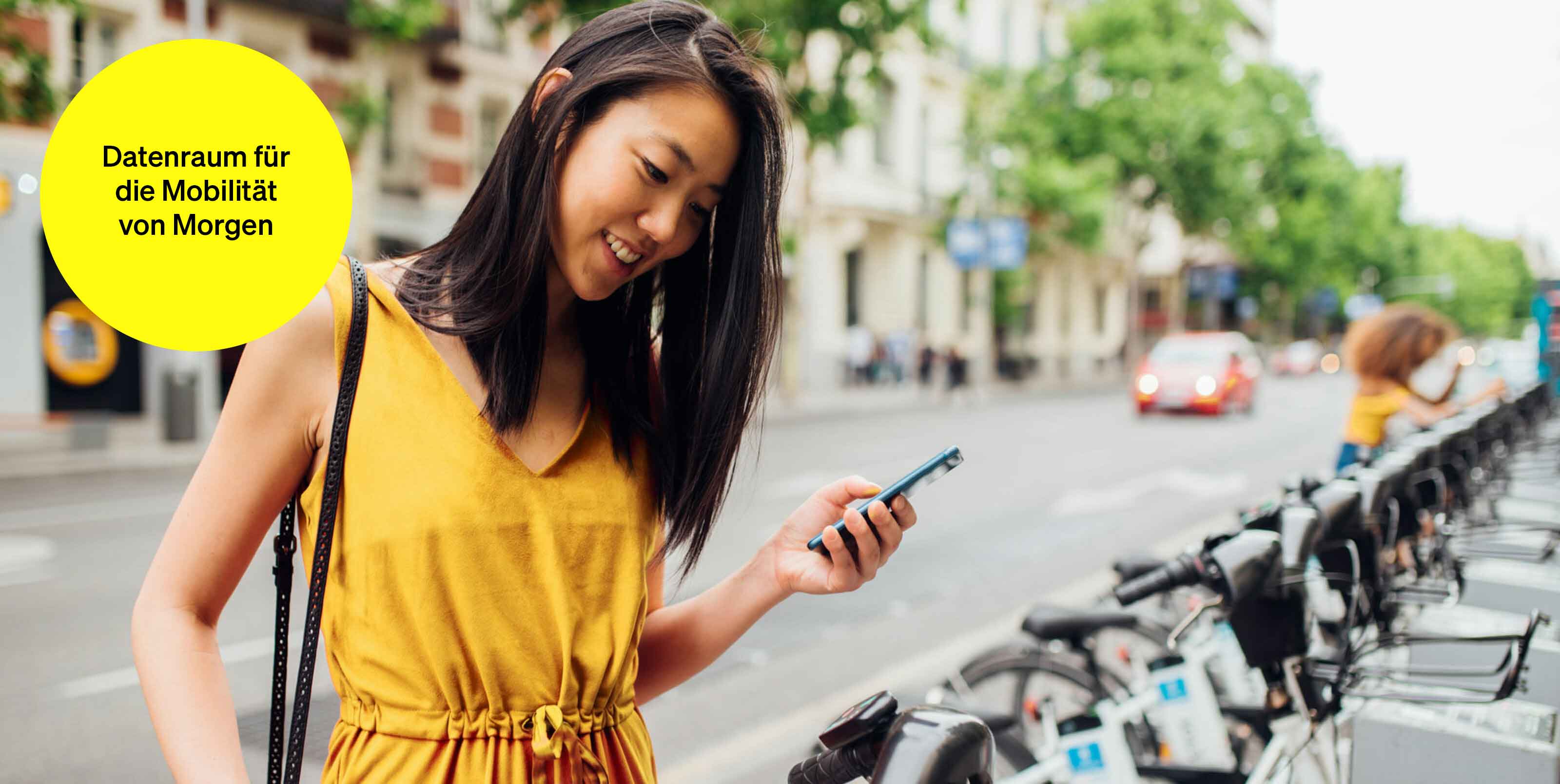 Frau mit Handy in der Hand an einer Bikesharing-Station – Textbaustein in runder Kachel: Datenraum für die Mobilität von Morgen