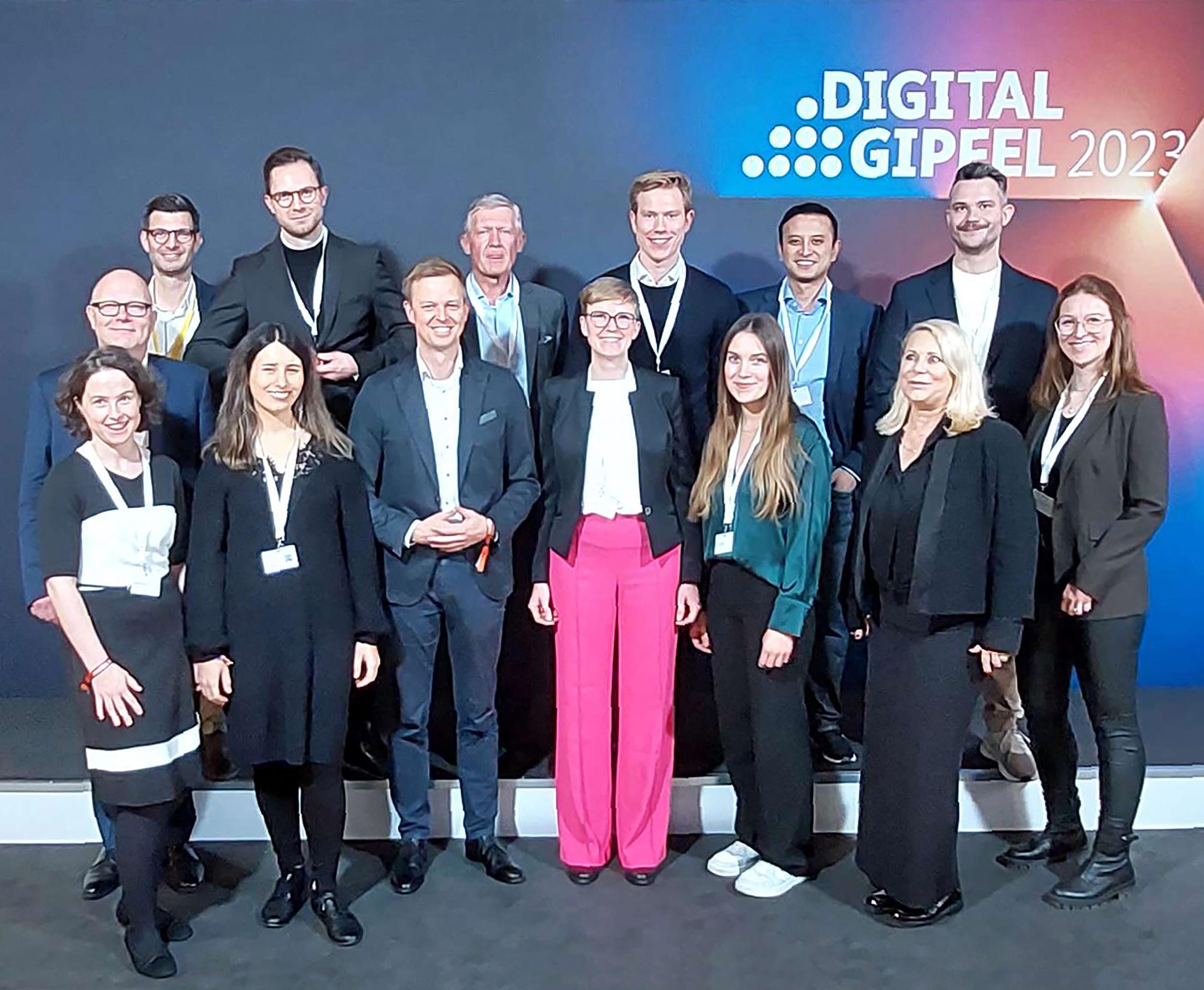 The picture shows a group of people posing and smiling for the camera. They are standing in front of a wall with the Digital Summit logo on it.