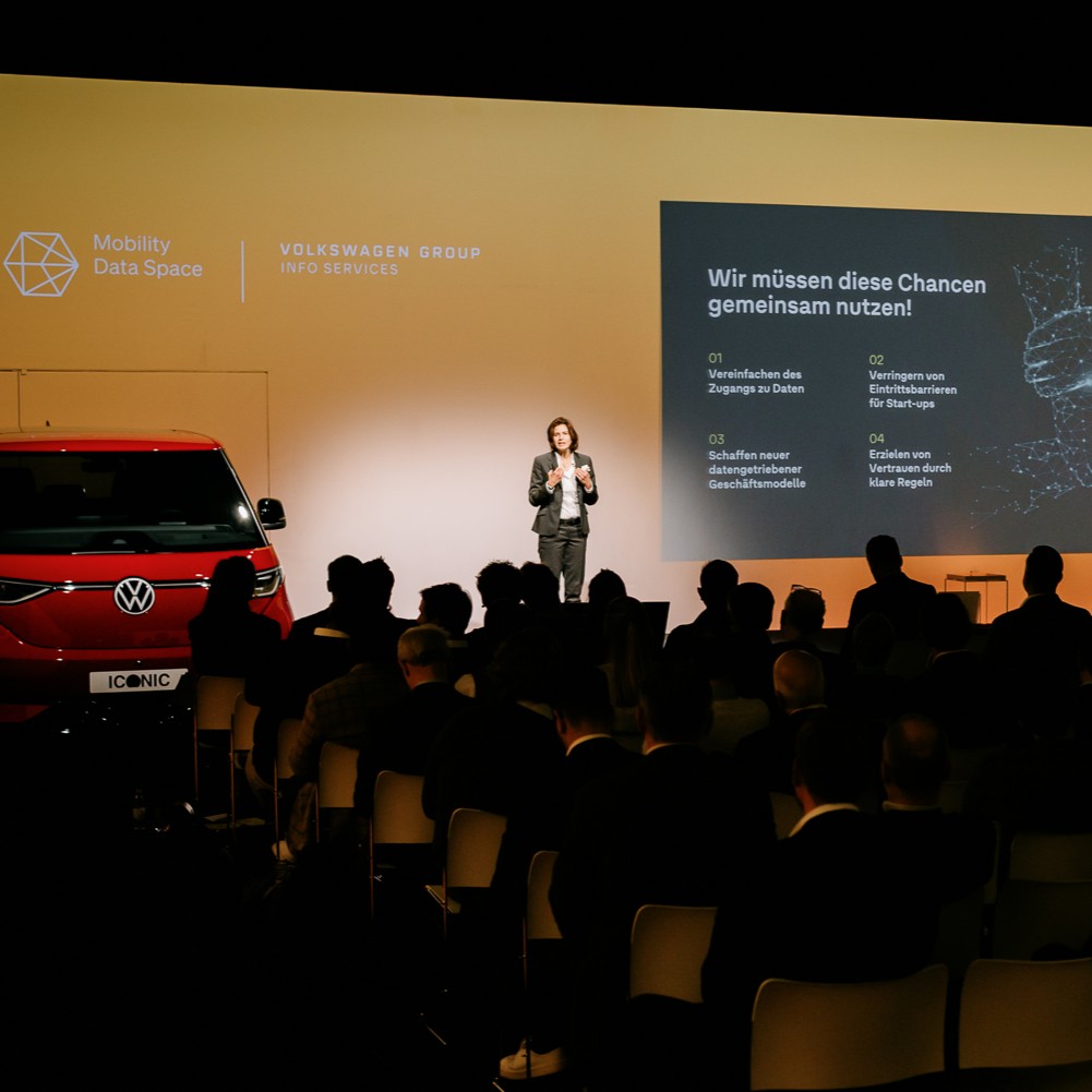 A person stands on a stage and gives a lecture to a large audience.